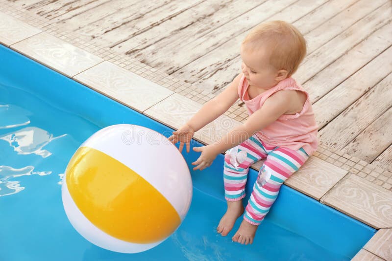 Little baby reaching for inflatable ball at swimming pool. Dangerous situation