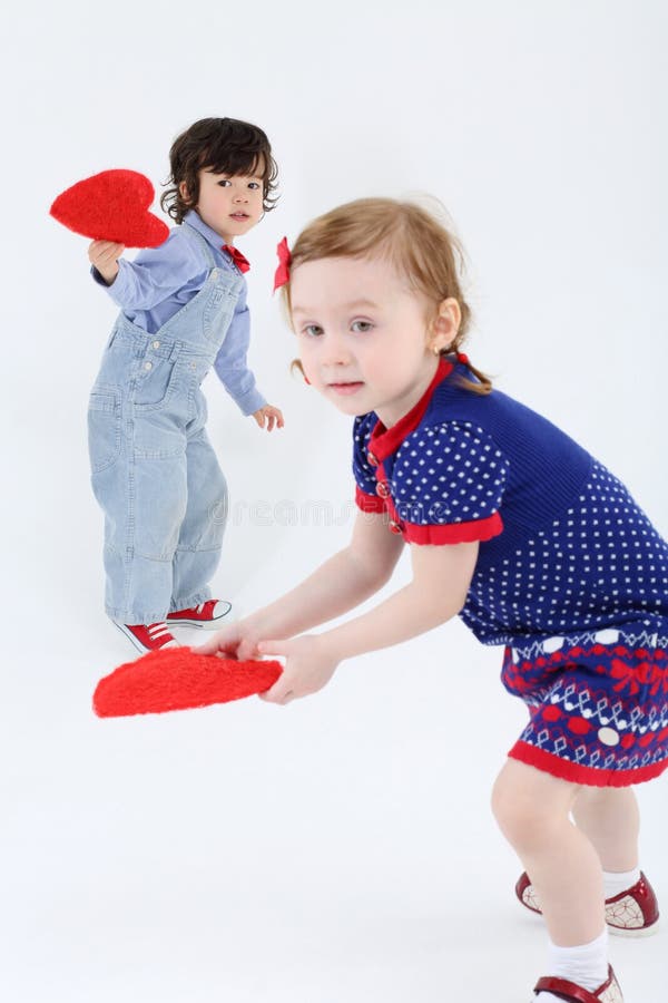 Little beautiful girl and boy stand and hold red hearts