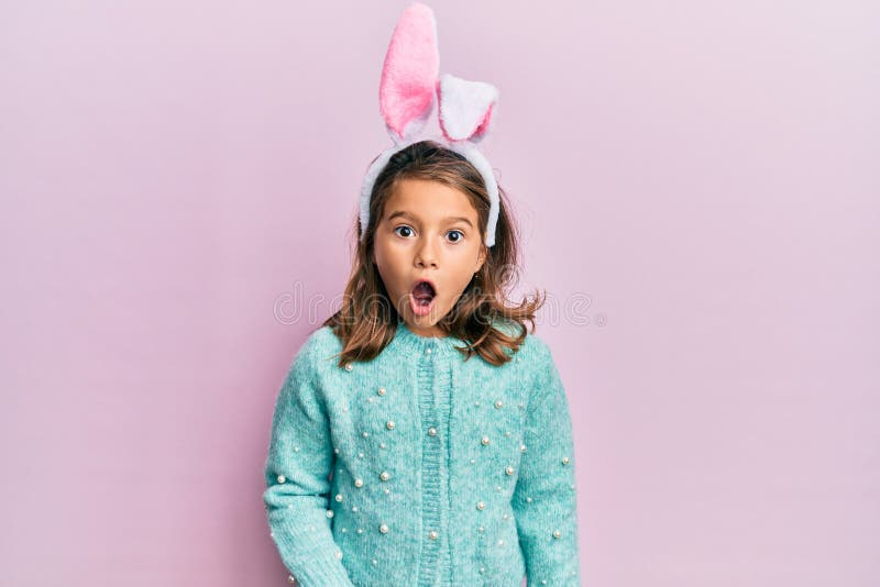 Little beautiful girl wearing cute easter bunny ears afraid and shocked with surprise expression, fear and excited face royalty free stock images