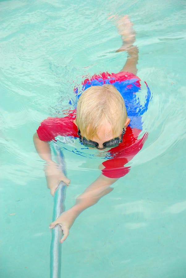 Un piccolo biondo Caucasica bambino ragazzo in costume da bagno per la pulizia della piscina con una spazzola sotto l'acqua, per essere pronto per la primavera.