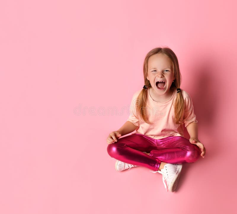 Little female in t-shirt, leggings and sneakers. She looking up , sitting on floor against pink background. Little blond woman in a t-shirt, leggings and white royalty free stock images Little female in t-shirt, leggings and sneakers. She looking up , sitting on floor against pink background. Little blond woman in a t-shirt, leggings and white royalty free stock images