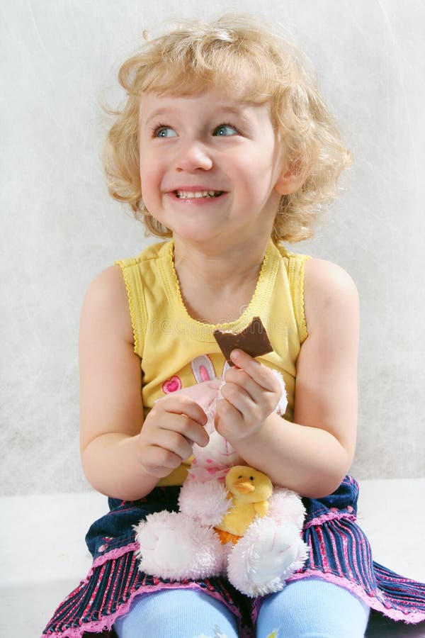 Little blonde curly girl eating chocolate with toy