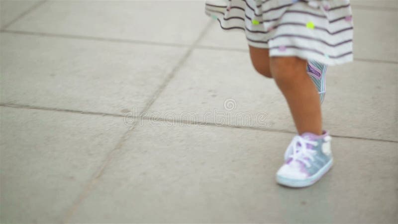 Little blonde girl in dress and blue sneakers is running to her mother wearing red shoes. View of the foots.