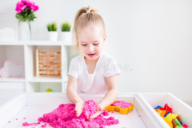 Little blonde girl playing with pink kinetic sand on a white table in a light room. Sensory development. Lessons in a kindergarten