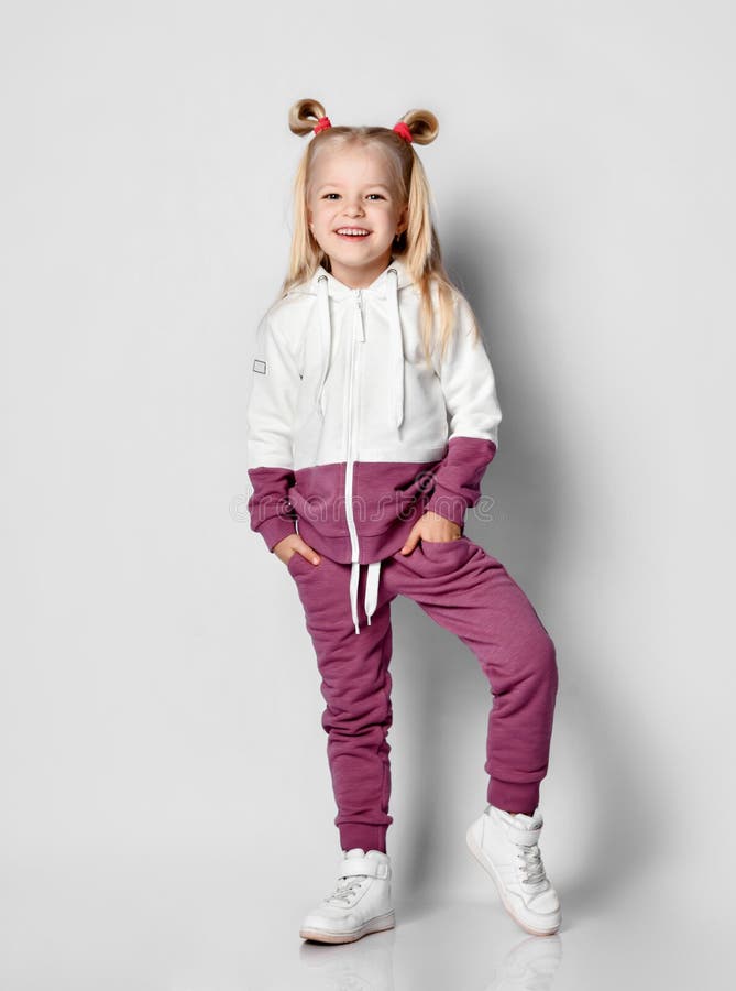 Little blonde girl in a sports suit posing on a gray background. Little blonde girl with a sly smile dressed in a fashionable sports suit posing on a gray stock photos Little blonde girl in a sports suit posing on a gray background. Little blonde girl with a sly smile dressed in a fashionable sports suit posing on a gray stock photos
