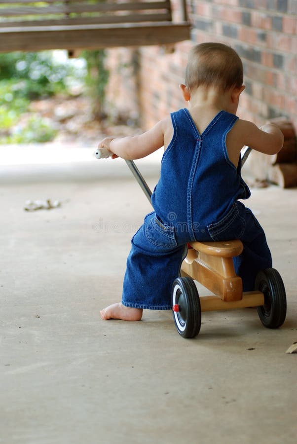 11 month old baby in blue jean overalls learning to ride an old wooden scooter. 11 month old baby in blue jean overalls learning to ride an old wooden scooter.