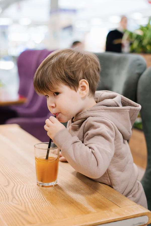 Little Boy Child Drinks Juice from a Straw while Sitting at a Table in