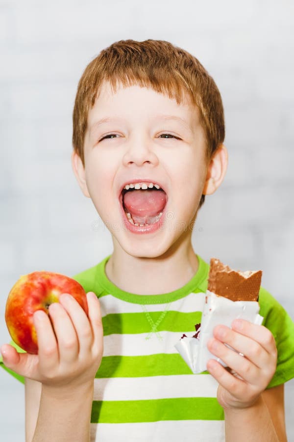 Little boy chooses chocolate or apple on a light background in the st