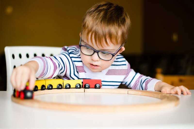 Little boy in the glasses with syndrome dawn playing with wooden railways