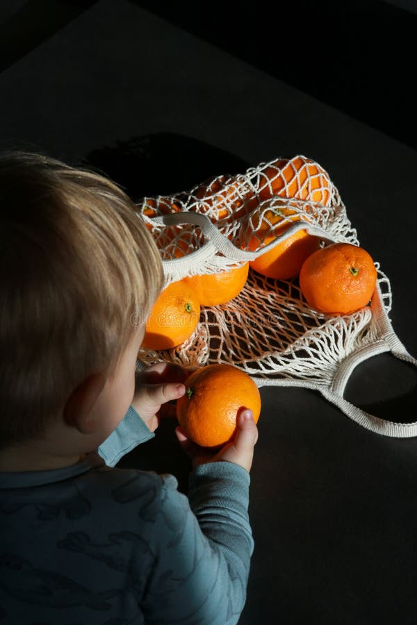 Child grabbing oranges from mesh bag, dark background stock image