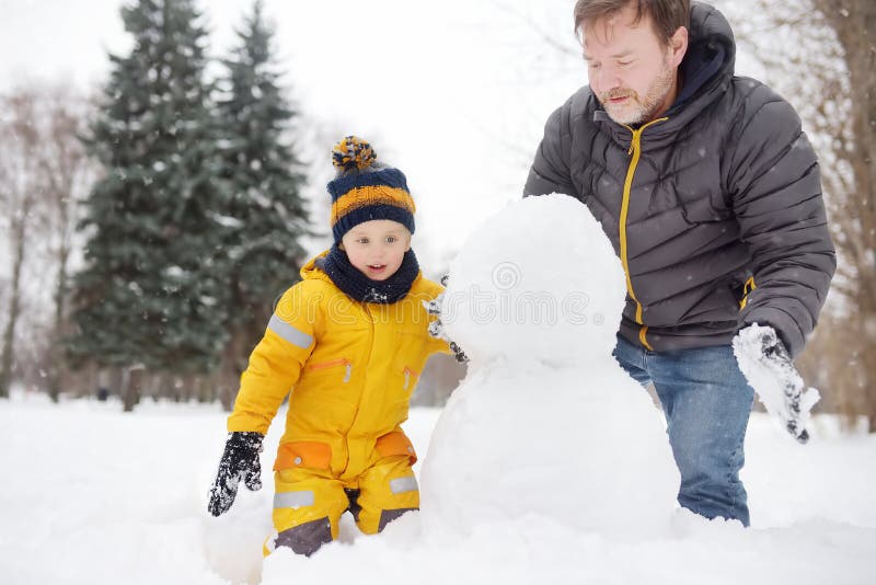 Little boy with his father building snowman in snowy park. Active outdoors leisure with children in winter royalty free stock photography Little boy with his father building snowman in snowy park. Active outdoors leisure with children in winter royalty free stock photography