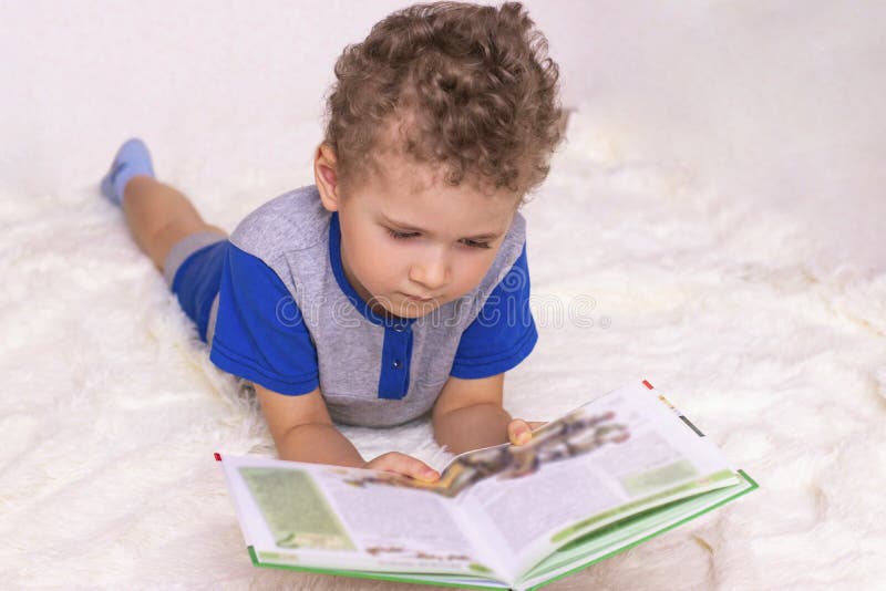 A Little Boy Lies On A Fluffy Bedspread And Reads A Book