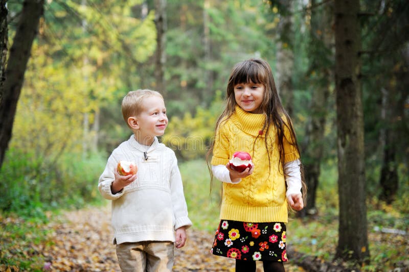 Little boy and little girl eating apples in forest