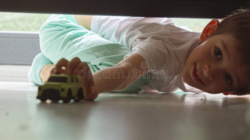 Little boy in pajamas looking under the bed and searching for lost toy car