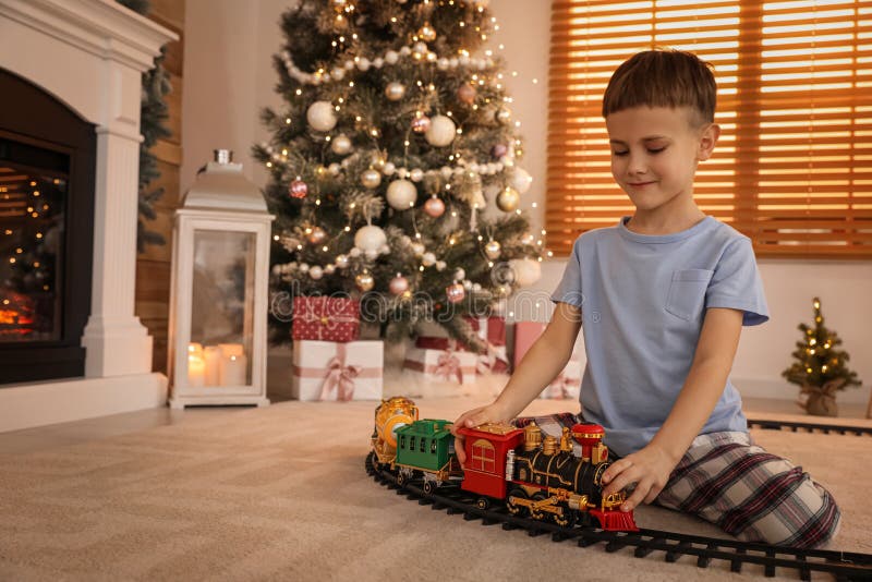 Little boy playing with colorful train toy in room decorated for Christmas