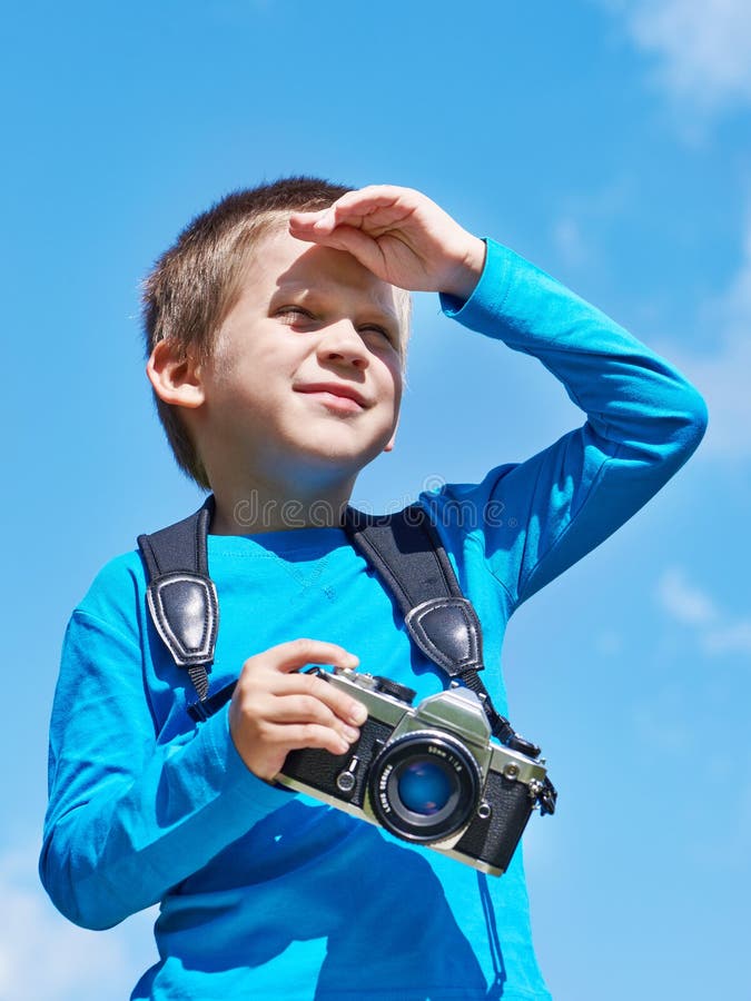 Little boy with retro camera on sky looks into distance