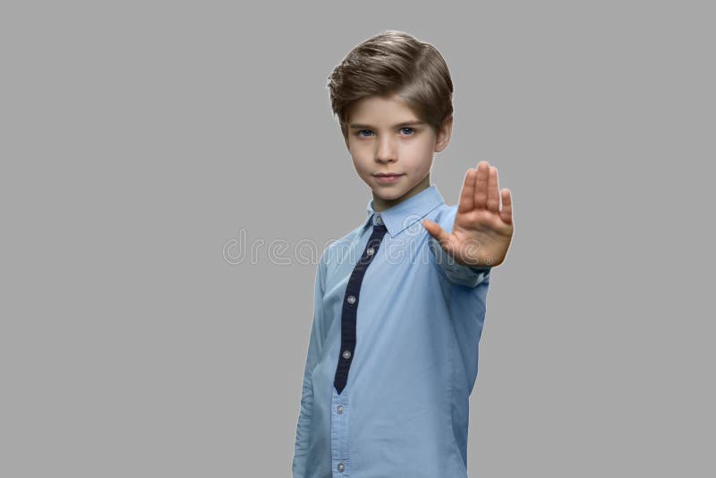 Little boy showing stop gesture on gray background.
