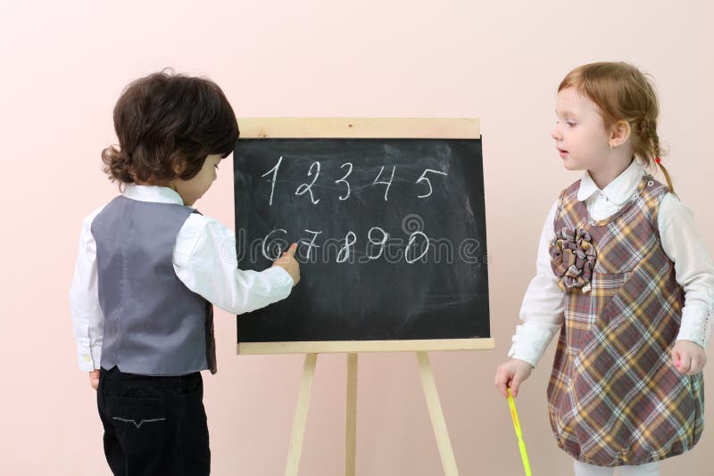 Little boy shows by finger figures at chalkboard for cute girl