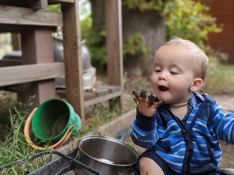 Little boy sitting on the ground looking at his muddy hand