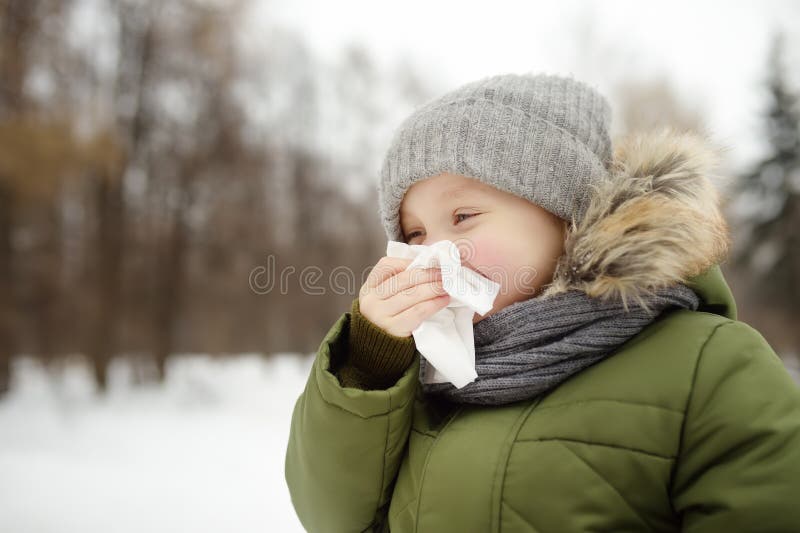 Little boy sneezing and wipes nose with napkin during walking in winter park. Flu season and cold rhinitis. Allergic kid stock images Little boy sneezing and wipes nose with napkin during walking in winter park. Flu season and cold rhinitis. Allergic kid stock images