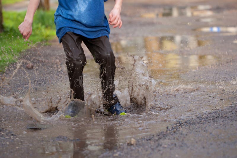 Little boy splashing in a mud puddle, jumping into a puddle