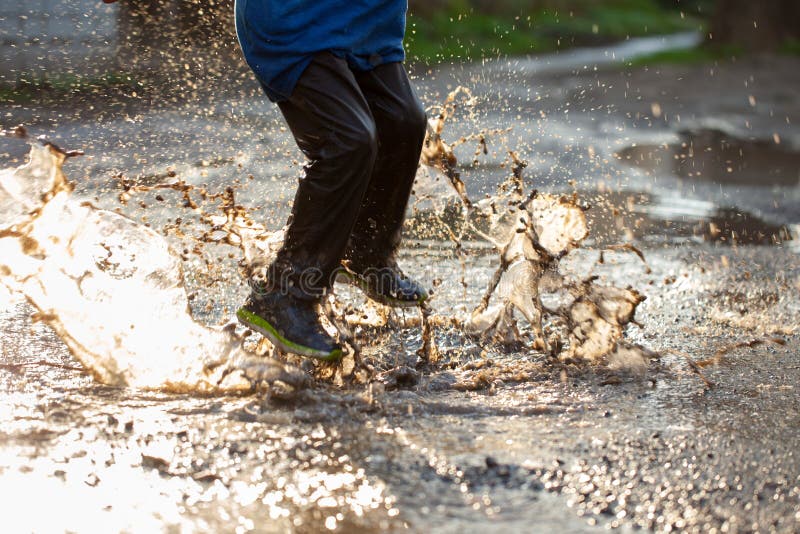 Little boy splashing in a mud puddle, jumping into a puddle