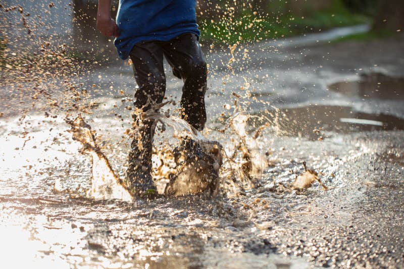 Little boy splashing in a mud puddle, jumping into a puddle