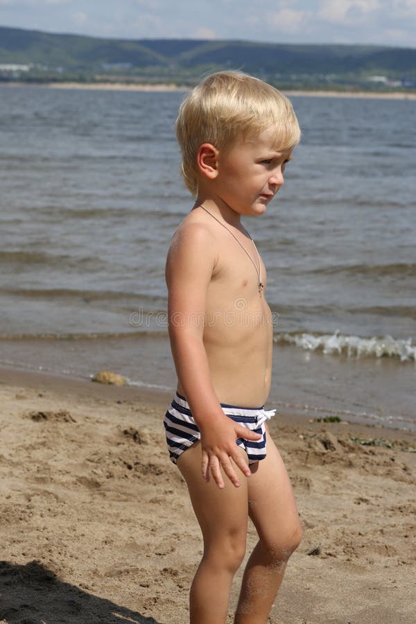 Little boy standing on the beach near the river