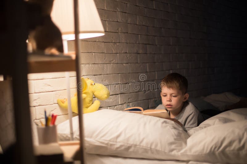 Little Boy sveglio che legge a letto fotografia stock libera da diritti Little Boy sveglio che legge a letto fotografia stock libera da diritti