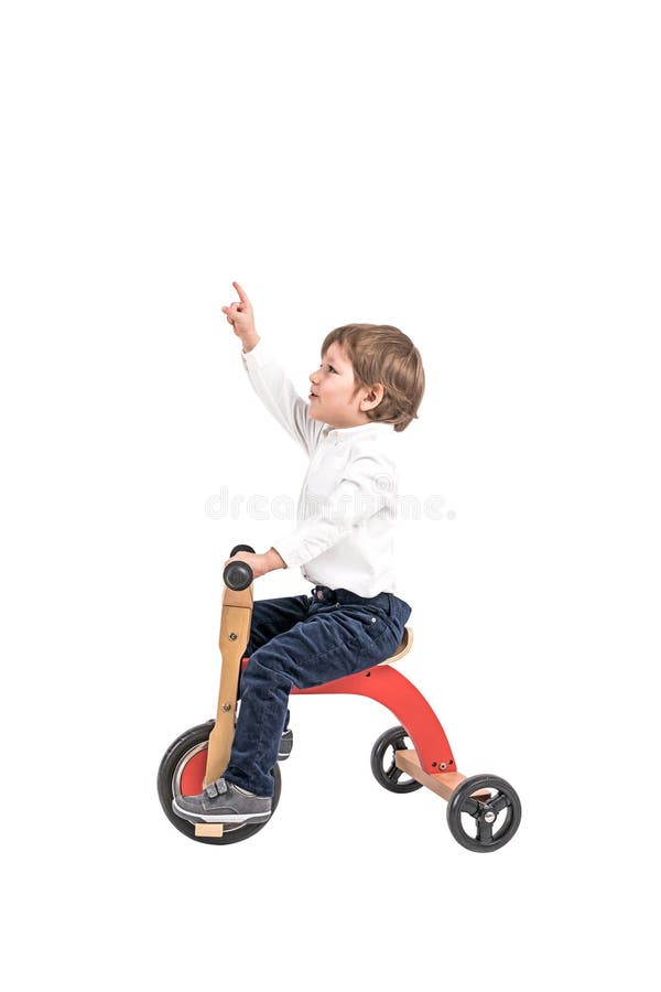 Isolated portrait of adorable little boy in white shirt and jeans riding tricycle and pointing upwards. Concept of childhood and business. Isolated portrait of adorable little boy in white shirt and jeans riding tricycle and pointing upwards. Concept of childhood and business