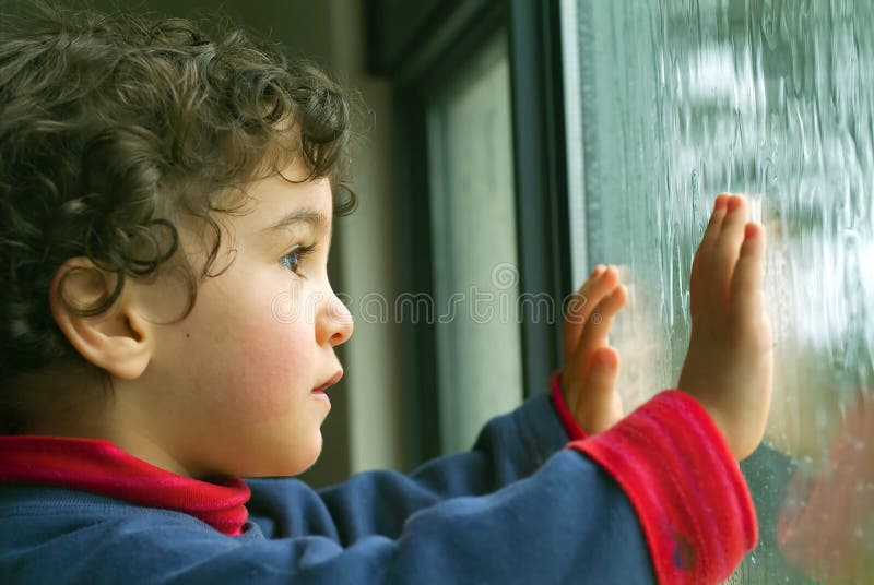 Bambino a guardare la pioggia dalla finestra.