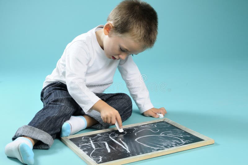 Little boy writing with chalk on black board