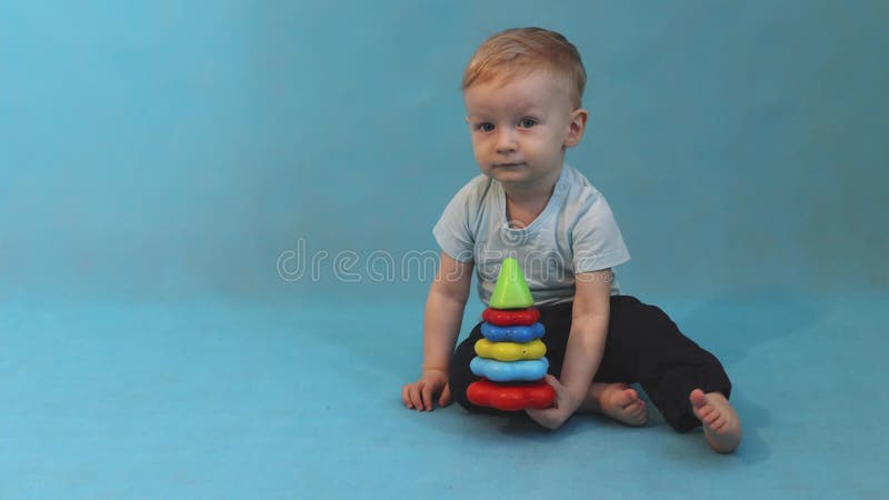 Little boy, 1 year old, playing with a multi-colored pyramid sitting on a blue background, soft focus.