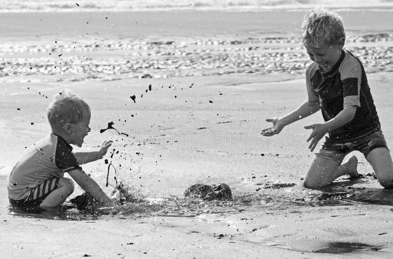 Two little boys who are brothers are having a great time out for the day at the seaside beach playing in the puddles and splashing the black sand and water at each other, smiling and laughing.nThe children give the perfect example how the simple pleasures of life are always the best moments of living.nTaken with permission.nEditorial content only. Two little boys who are brothers are having a great time out for the day at the seaside beach playing in the puddles and splashing the black sand and water at each other, smiling and laughing.nThe children give the perfect example how the simple pleasures of life are always the best moments of living.nTaken with permission.nEditorial content only.