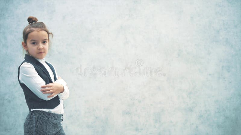 Little business lady stands on a gray background. During this, turning half a turn. Look into the camera. Twins