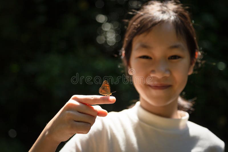 Little butterfly on the finger of an Asian girl,Cute girl learning near butterfly in the forest