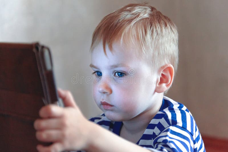 Little caucasian baby boy uses a tablet, seeing to the screen. Children time spending, computerization of youngsters.