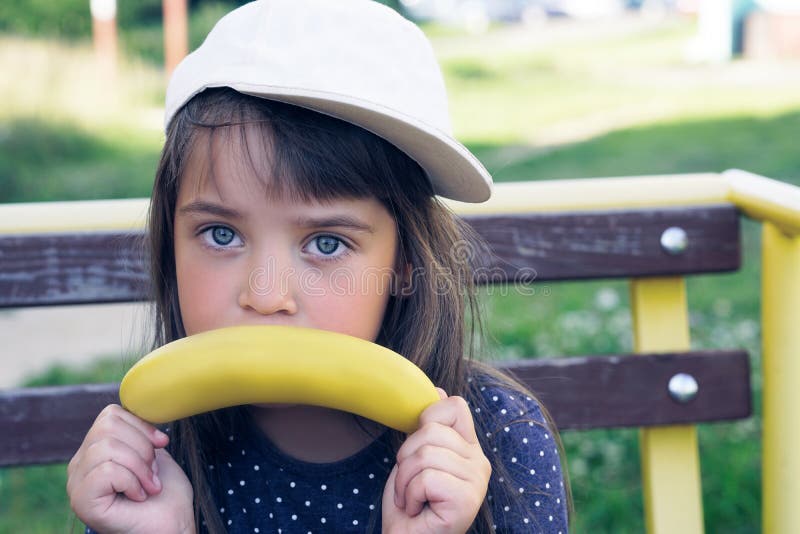 Little caucasian girl making sad gesture with banana over nature background. Fun and healthy eating.