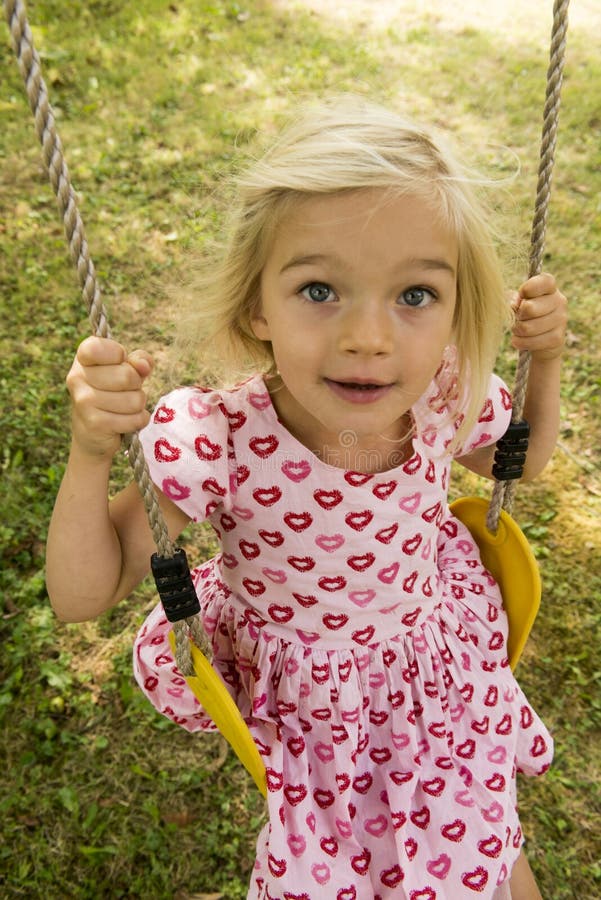 Little child blond girl having fun on a swing outdoor. Summer playground