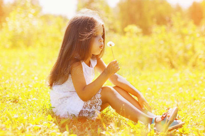Little child blowing dandelion in sunny summer day