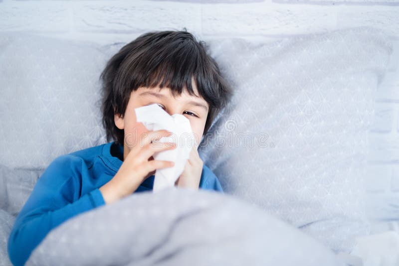 Little child boy blow his nose. Sick child with napkin in bed. Allergic kid, flu season. Kid with cold rhinitis, get cold