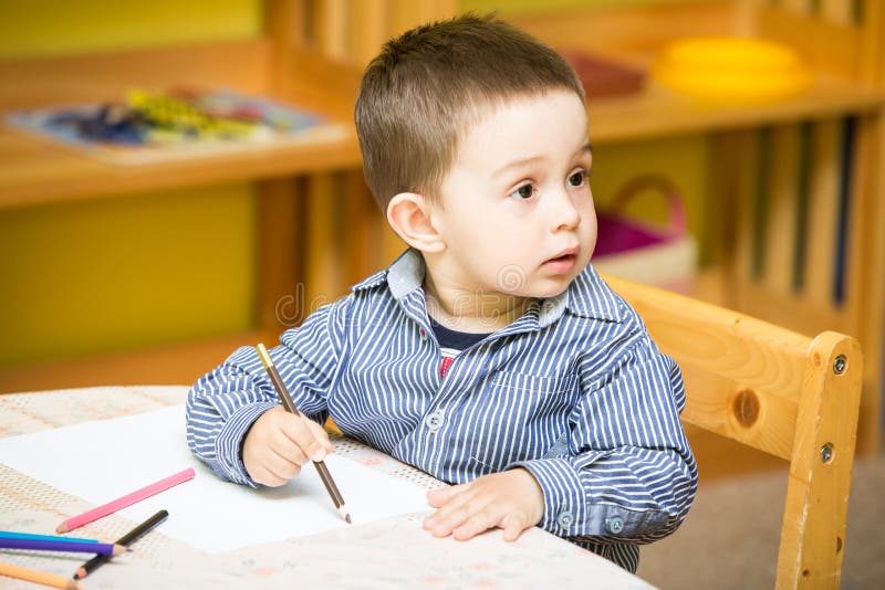 Little child boy drawing with colorful pencils in preschool at table in kindergarten