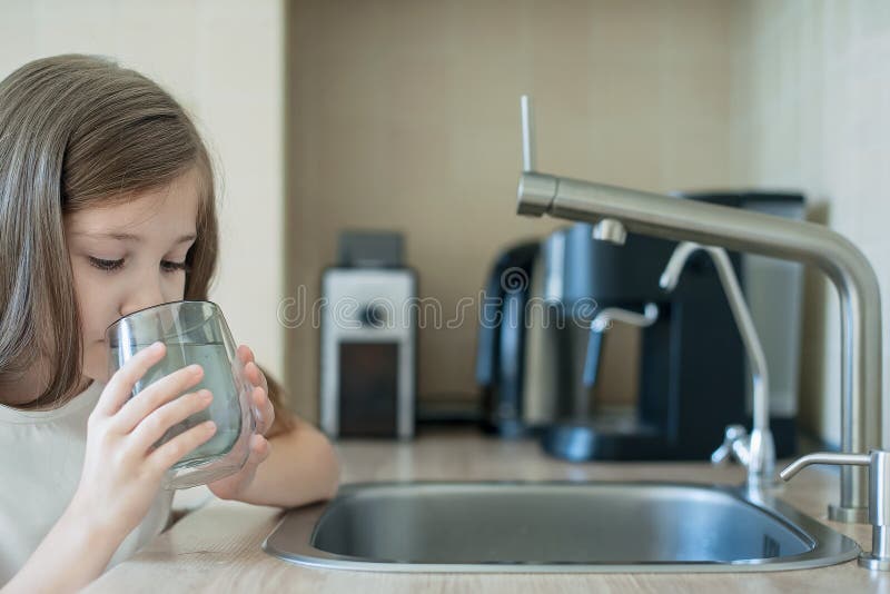 Little child is drinking fresh and pure tap water from glass. Water being poured into glass from kitchen tap. Zero waste and no