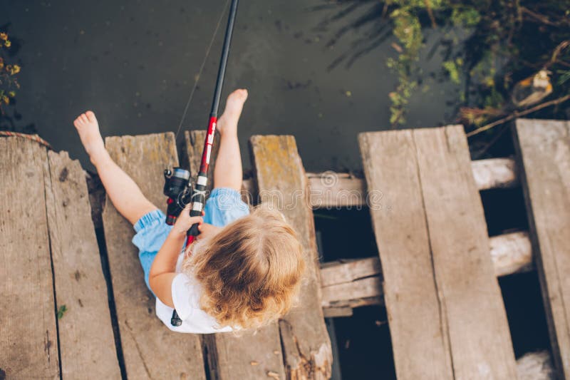 Little child fishing from wooden dock on lake