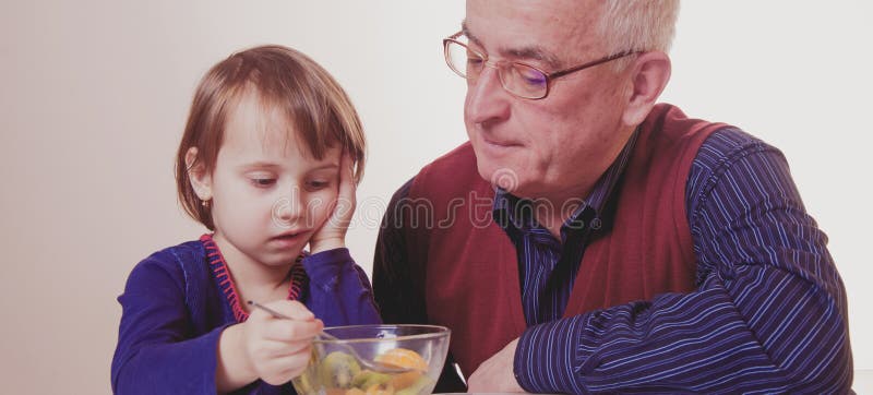 Little child girl does not want to eat and has no appetite. Grandpa feeding his grandchild with fruits salad