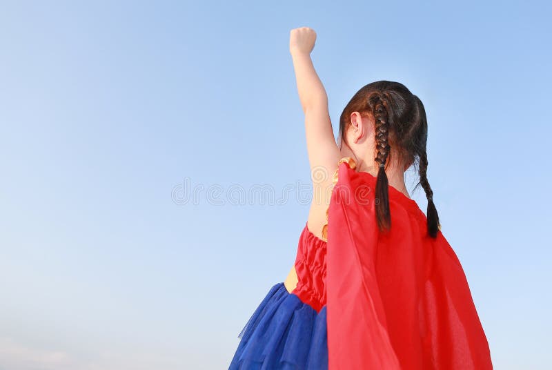 Little child girl Superhero in a gesture to fly on clear blue sky background. Kid super hero concept