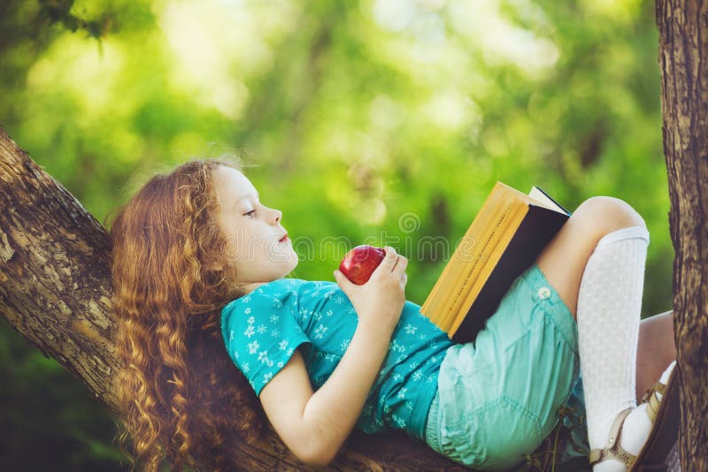 Little child lying on large tree and reads the book.