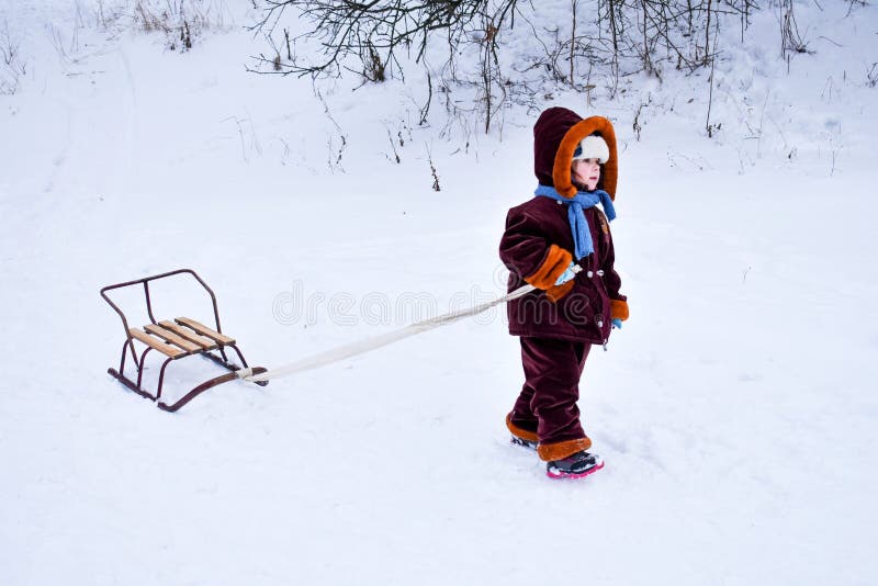 Little child pulling a sled in the snow. The kid is riding on a sleigh. Children play outside in the snow, children ride. Outdoor fun for family Christmas vacations