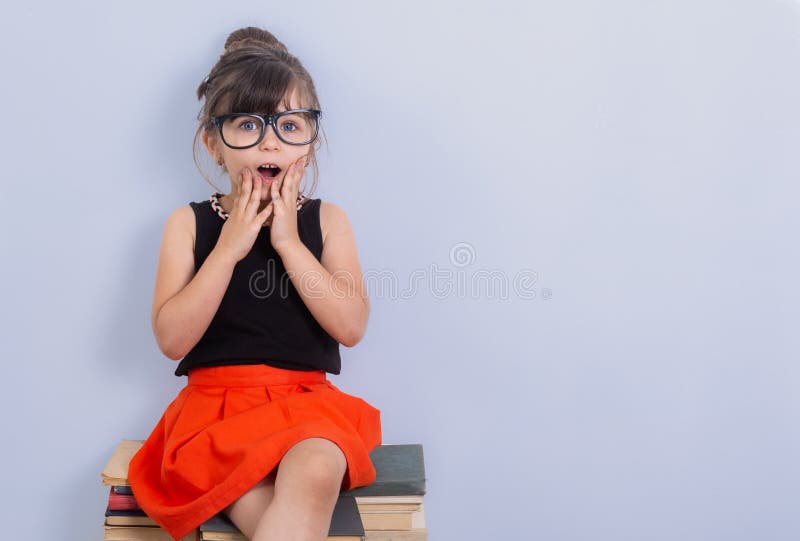 Little child reading book and in bewilderment covers mouth. Kid with glasses sitting on books. royalty free stock photos Little child reading book and in bewilderment covers mouth. Kid with glasses sitting on books. royalty free stock photos