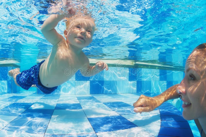 Little child swimming underwater in pool with mother